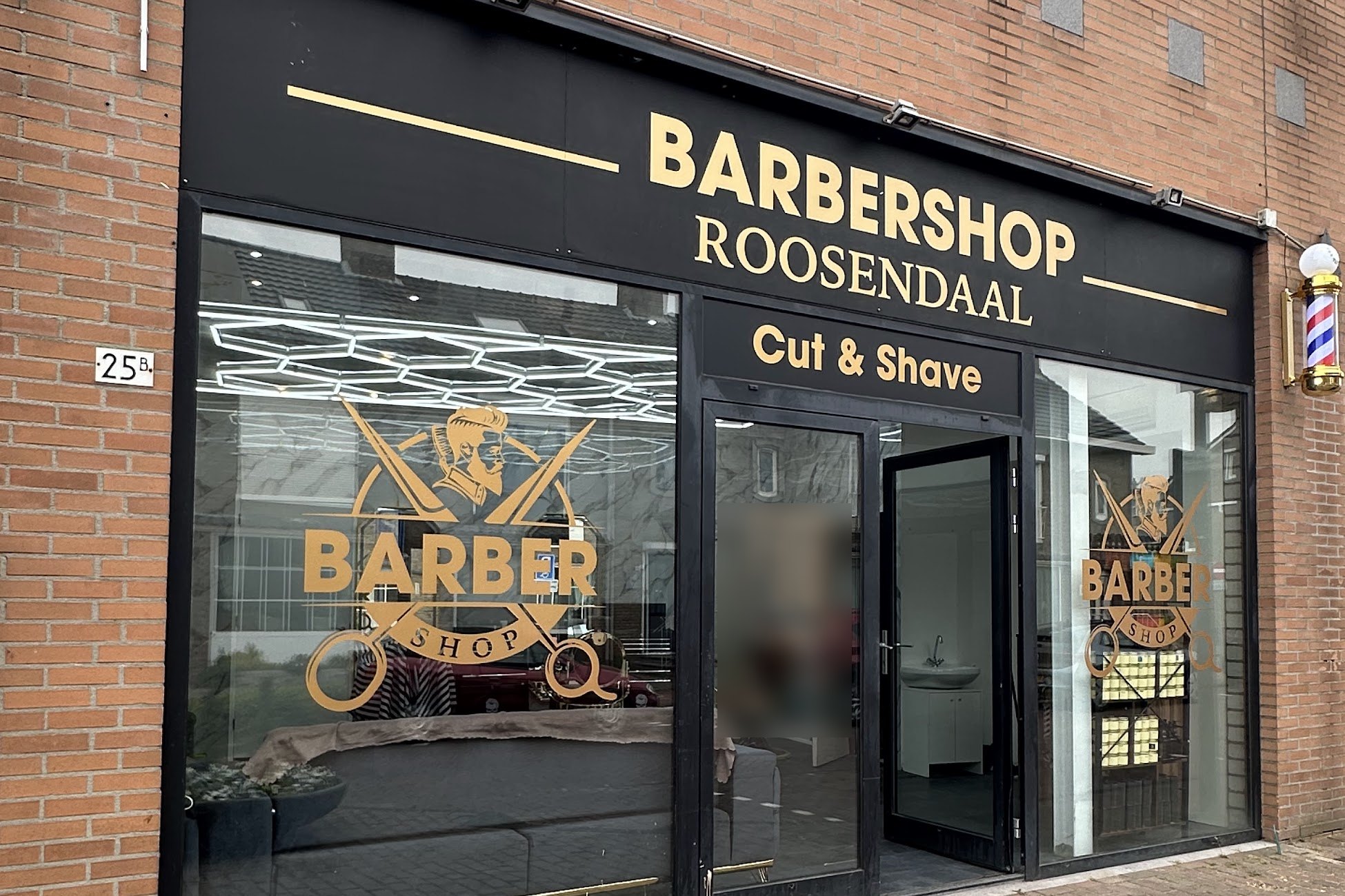 De gevel van Barbershop Roosendaal aan de Roselaar 25B: gouden letters Barbershop Roosendaal, Cut & Shave op een zwarte gevel, met de barberpaal naast de deur