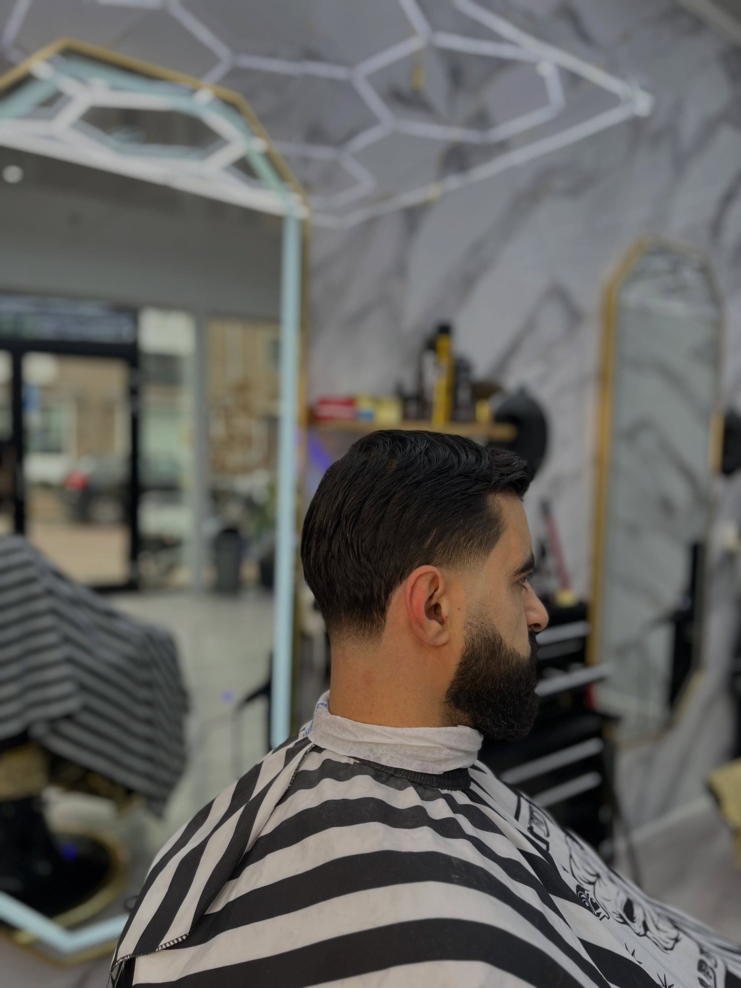 Klant in profiel met een fade en een bijgewerkte baard, de zaak onscherp op de achtergrond
